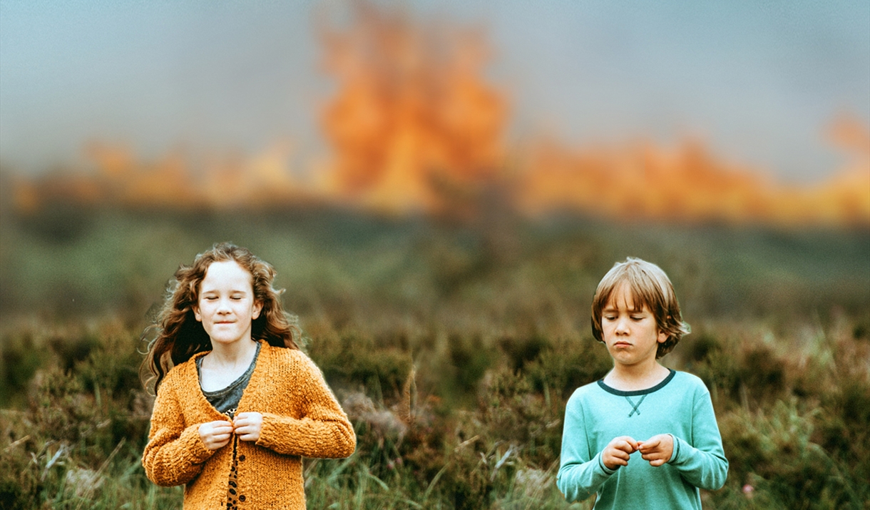 Two children in a field.  There are flames in the distance.