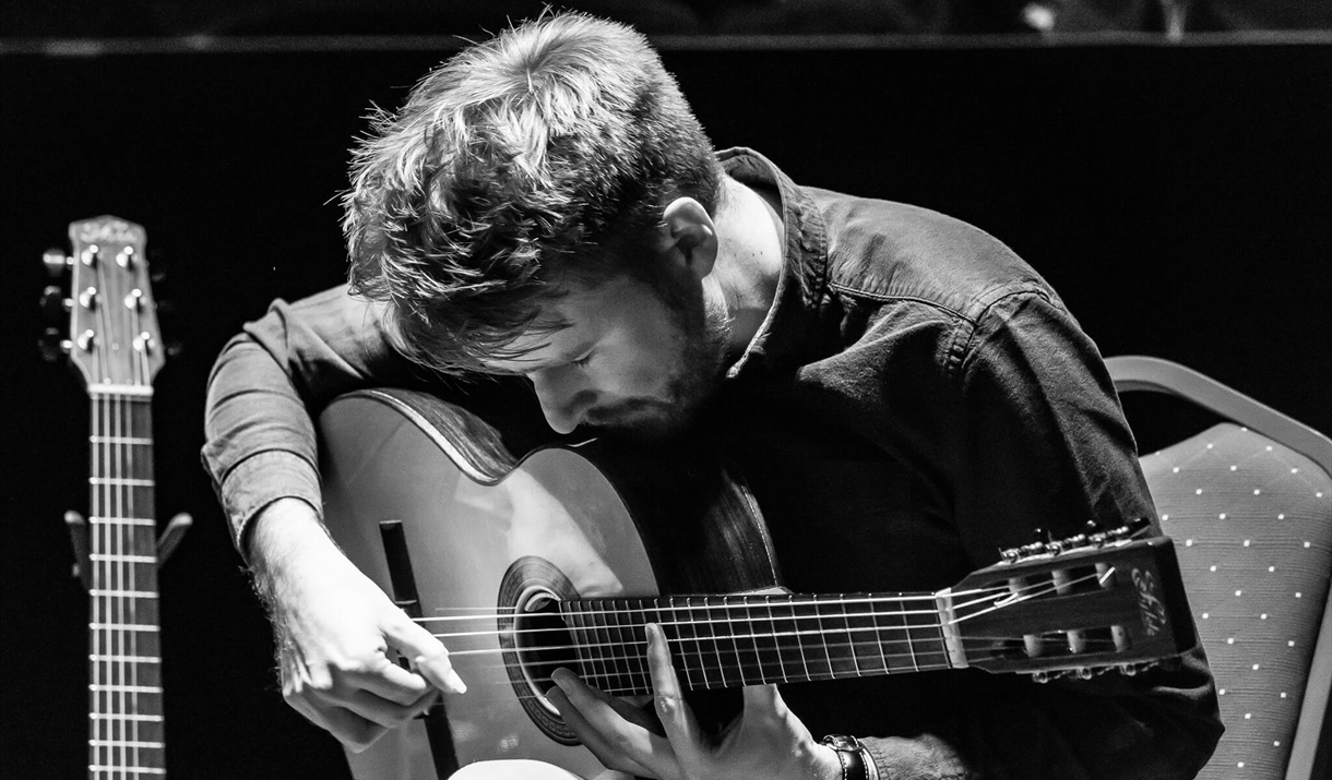 a black and white photographs of will mcnicol playing acoustic guitar