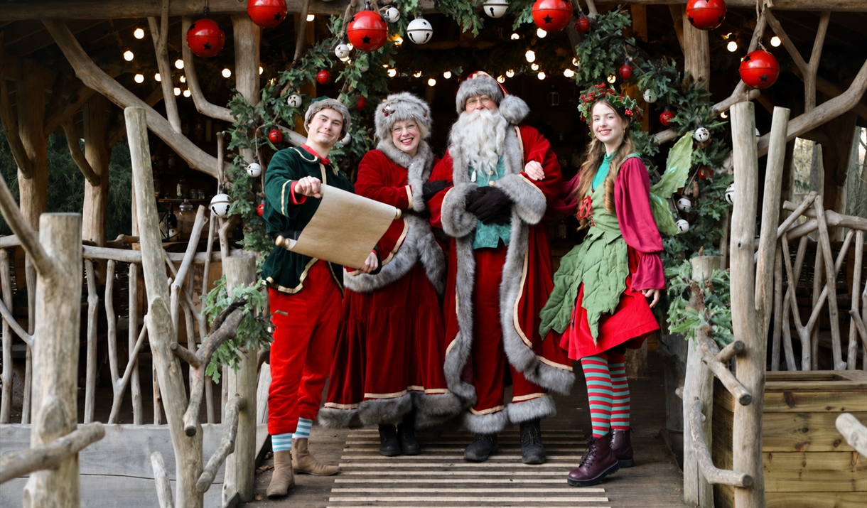Father Christmas and Mother Christmas with two festive elves standing beneath a decorated Christmas archway at Audley End Enchanted Railway.