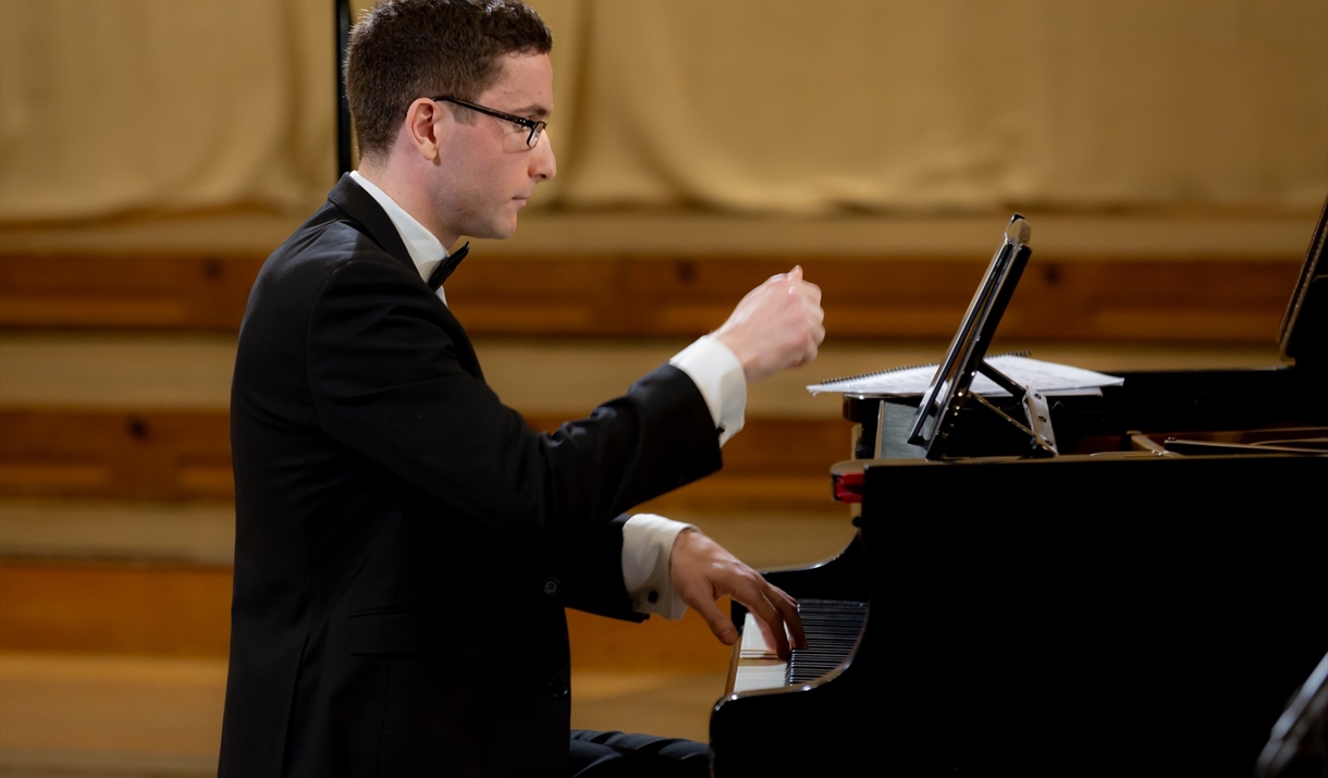 A man in a tuxedo plays a grand piano