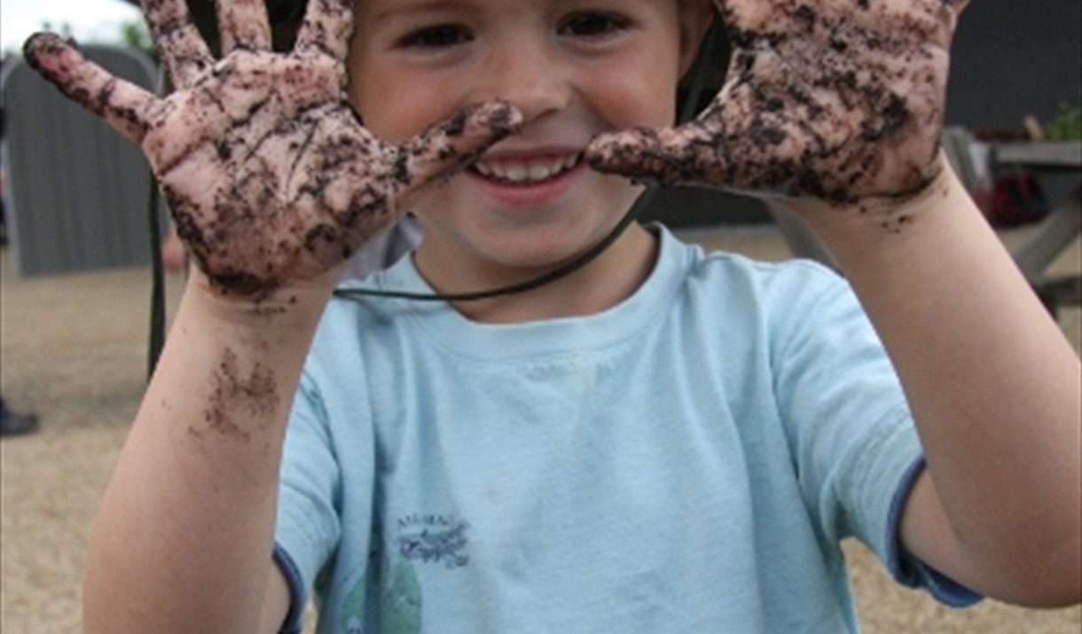 A young boy, with a big grin, holds up his muddy hands during an event at Rainham Marshes