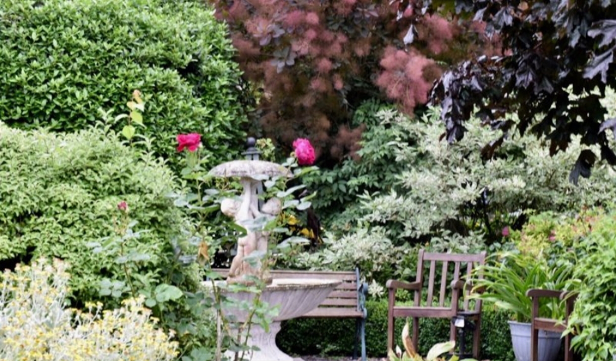 Beautiful garden with statues, bench and flowers