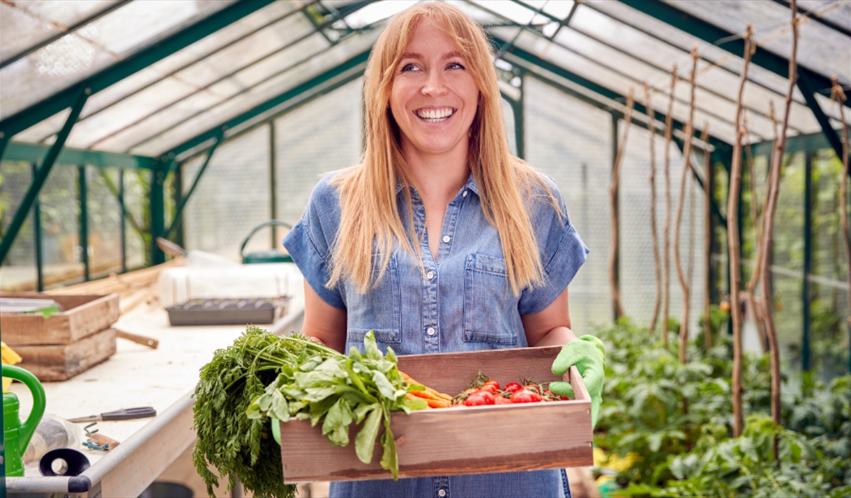 Smiling woman standing in greenhouse with box of home grown vegetables