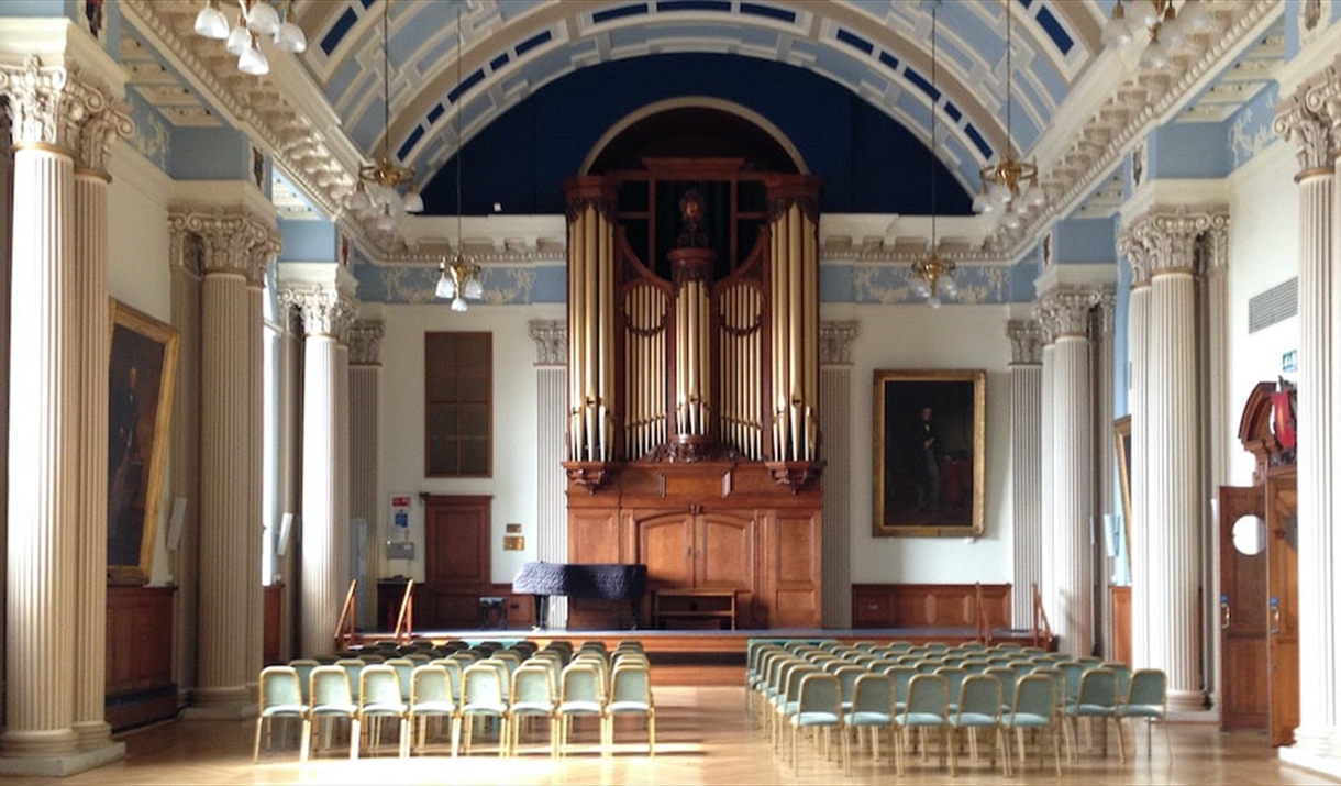 A grand hall with rows of chairs facing a stage, dominated by a large pipe organ.