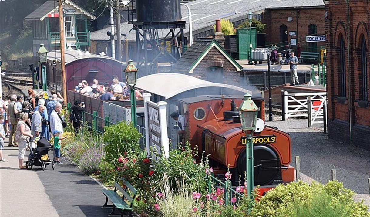 A red and black steam train with people aboad
