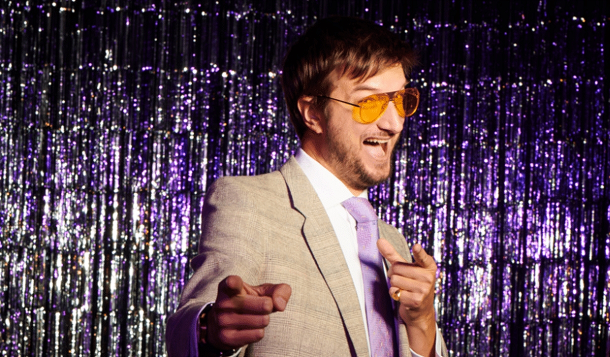 Man in yellow glasses with a purple glitter backdrop