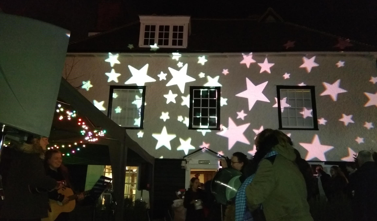 Epping Forest District Museum is lit up by bright star projections. Happy crowds stand in front.