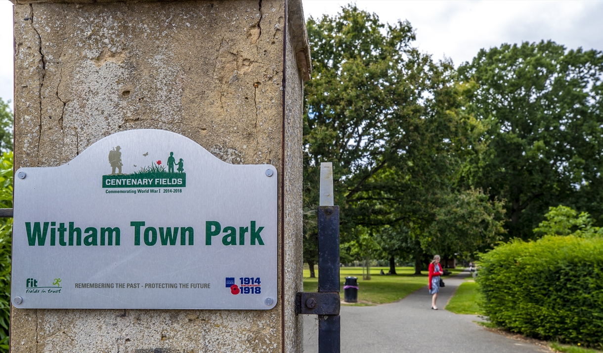 sign showing witham town park on the gate plus woman walking in the park