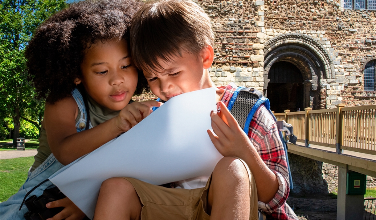 two children sitting outside colchester castle park, looking at a piece of paper