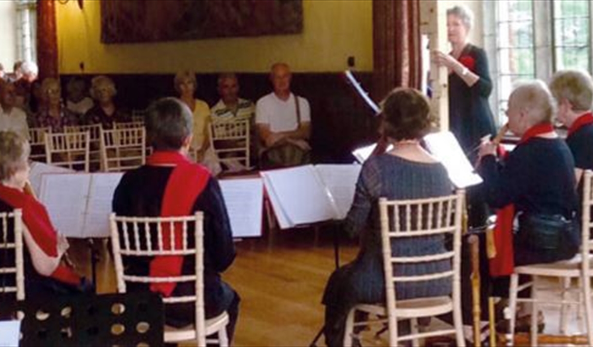 six musicians play to a small audience in a wood panelled hall with a large window