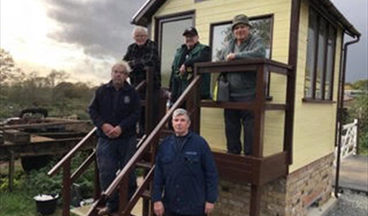 Five men stand outside a wooden hut.