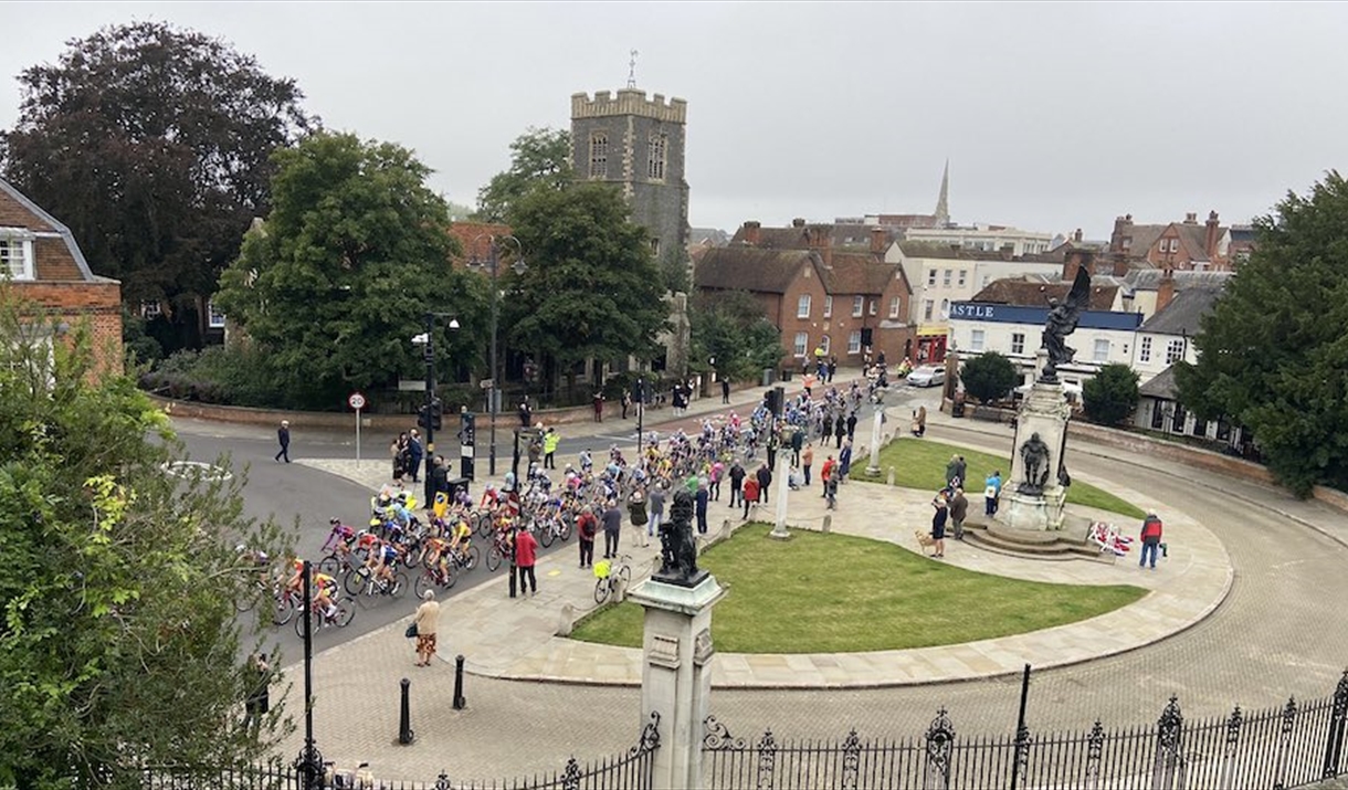 A large group of cyclists race past Colchester's war memorial