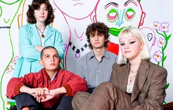 The four members of Anorak Patch pose in front of a mural.