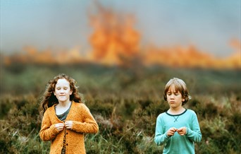 Two children in a field.  There are flames in the distance.