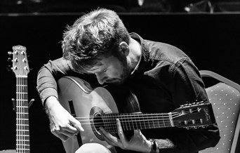 a black and white photographs of will mcnicol playing acoustic guitar