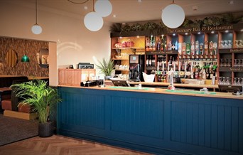 A modern bar with a blue, wooden front and a selection of drinks along the back wall