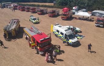 Field with a combine harvester, fire engine, tractor, emergency vehicles and a horse