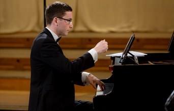 A man in a tuxedo plays a grand piano