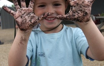 A young boy, with a big grin, holds up his muddy hands during an event at Rainham Marshes