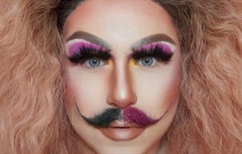 A drag artist with wild blonde hair wearing false eyelashes, pink eyeshadow and a mustache