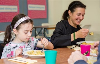 An adult woman and child eating a plate of food and smiling.