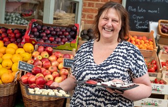 Female holding cheese samples in front of fruit and vegetable display