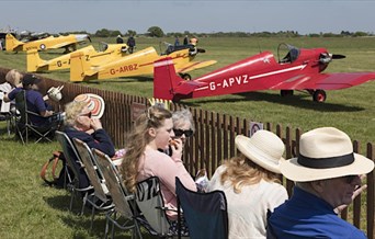 Row of people watching small yellow and red aircraft about to take off