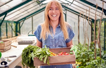 Smiling woman standing in greenhouse with box of home grown vegetables