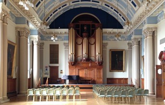 A grand hall with rows of chairs facing a stage, dominated by a large pipe organ.