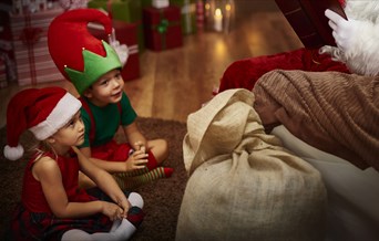 Two children in elf costumes sit at Santa's feet.