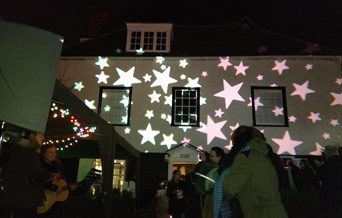 Epping Forest District Museum is lit up by bright star projections. Happy crowds stand in front.