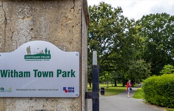 sign showing witham town park on the gate plus woman walking in the park