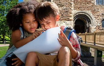 two children sitting outside colchester castle park, looking at a piece of paper