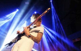 A woman, wearing white, plays electric guitar