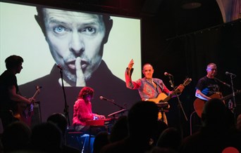 A live band performing in front of an image of David Bowie