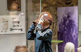 a child trying on a replica roman helmet in a museum