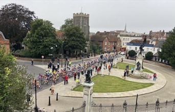 A large group of cyclists race past Colchester's war memorial