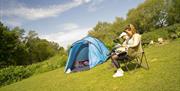 Blue tent set up on tent with with two people sat in camping chairs