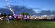 Music festival as the sun sets with festoon lights strung across the open space, large Eastern Electrics sign on metal frame