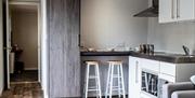 Kitchen area with sink and cooker, breakfast bar with stools and grey settee