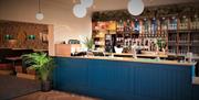 A modern bar with a blue, wooden front and a selection of drinks along the back wall