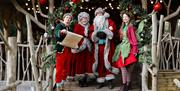 Father Christmas and Mother Christmas with two festive elves standing beneath a decorated Christmas archway at Audley End Enchanted Railway.