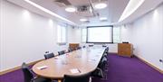 Meeting room laid out with long table and chairs around it.