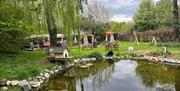 Pond surrounded by picnic benches, willow trees, and the pink Galloping Grind horsebox café in the background