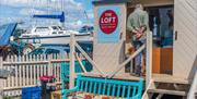 Outside of The Loft Tea by the Sea with blue bench seat and boats in the background