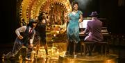 Production photograph of Ain't Misbehavin', three performers dance and sing around an upright piano.