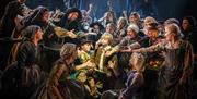 Production photograph from Oliver!, crowd of performers all gesture towards Oliver and Dodger.