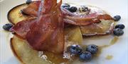 Home made pancakes with Norfolk Applewood smoked bacon, blueberries and icing sugar for breakfast at Piglets