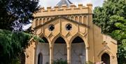 A cream coloured ancient-looking building called a folly, situated within an established garden