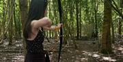 Woman with long hair shooting a recurve bow at a 3D target in a sunny woodland